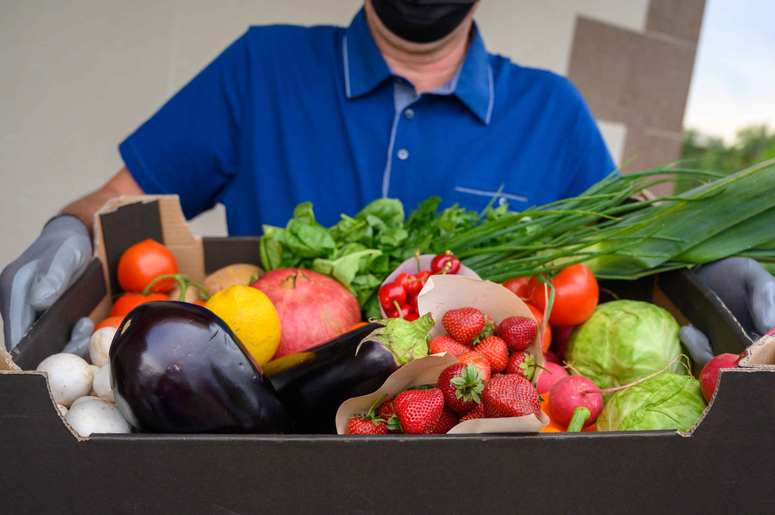 delivery man in mask holding fresh vegetables full box. home delivery during quarantine